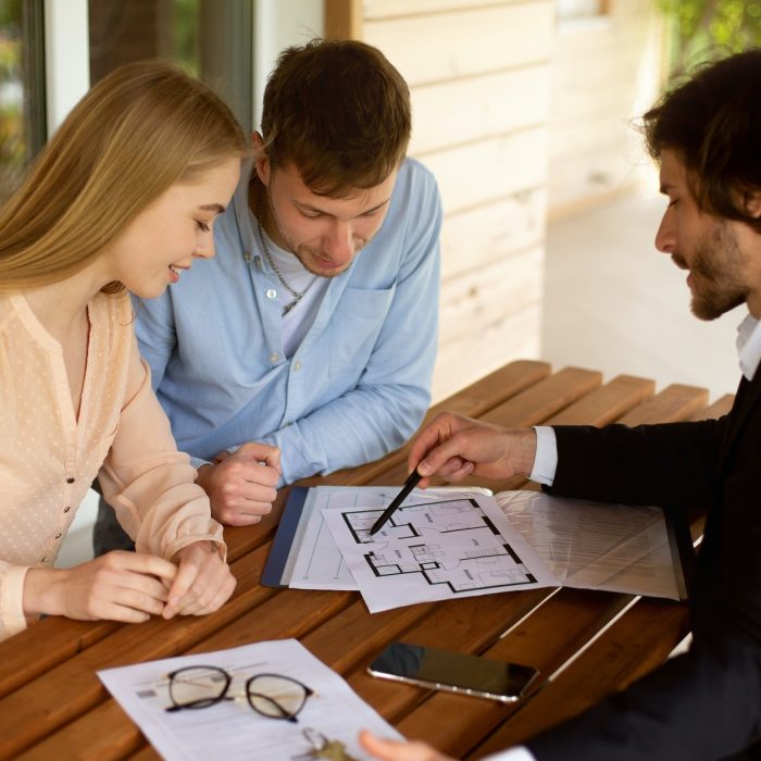 Property manager showing house plan to his clients at table on porch